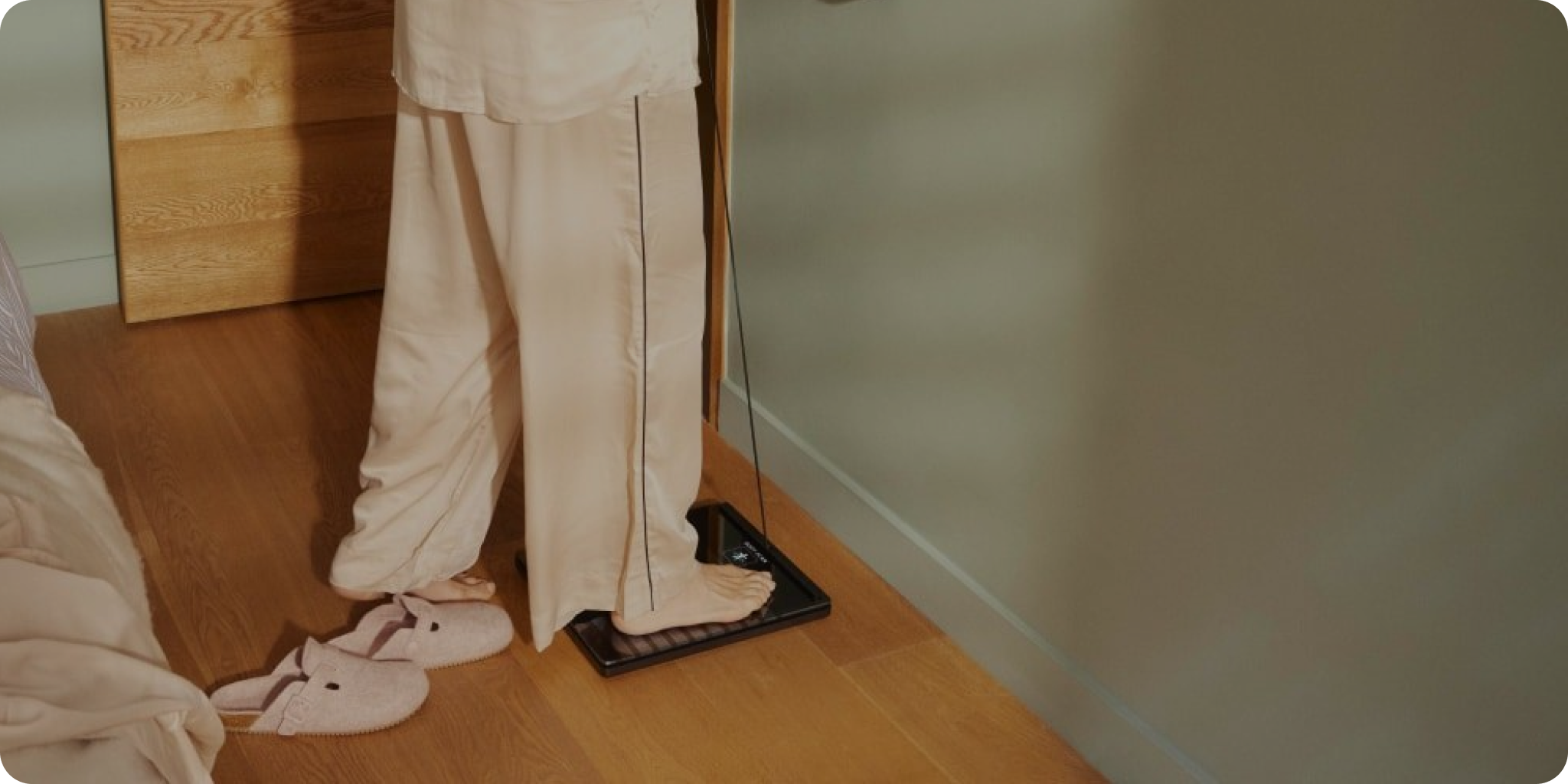 Person in neutral pyjamas standing on a Withings scale in a softly lit bedroom.